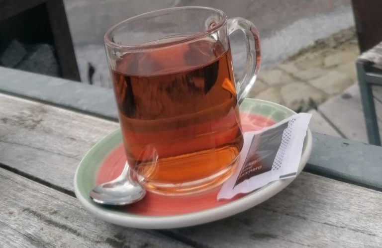 Ein Glas Tee auf einem Unterteller mit einem Löffel und einem Zuckersäckchen.