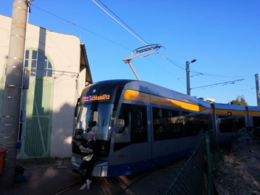 Moderne Straßenbahn an einer Gleisanlage, blauer Himmel im Hintergrund.