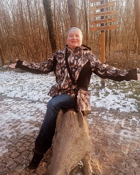 Tanzen ─ auch im sitzen Frau sitzt auf einem Baumstumpf und breitet ihre Arme in einer bewaldeten Umgebung aus.