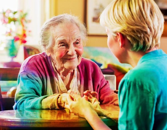 Eine ältere Frau lächelt, während sie die Hände einer jüngeren Person hält.