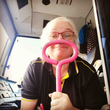 Lächelnde Person hält einen pinken Haken in einem Fahrzeug.