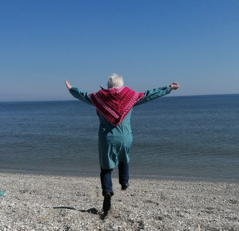 Eine Person mit grauen Haaren springt fröhlich am Strand entlang.