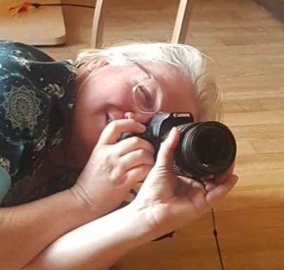 Eine lächelnde Person liegt auf dem Boden und fotografiert mit einer Kamera.